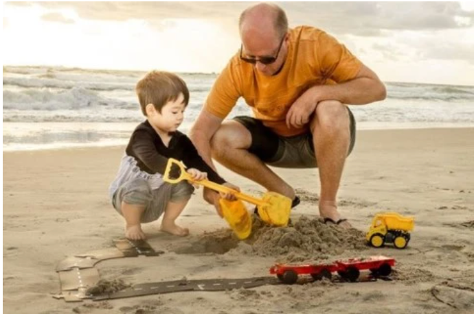 Father and son playing cars on the beach